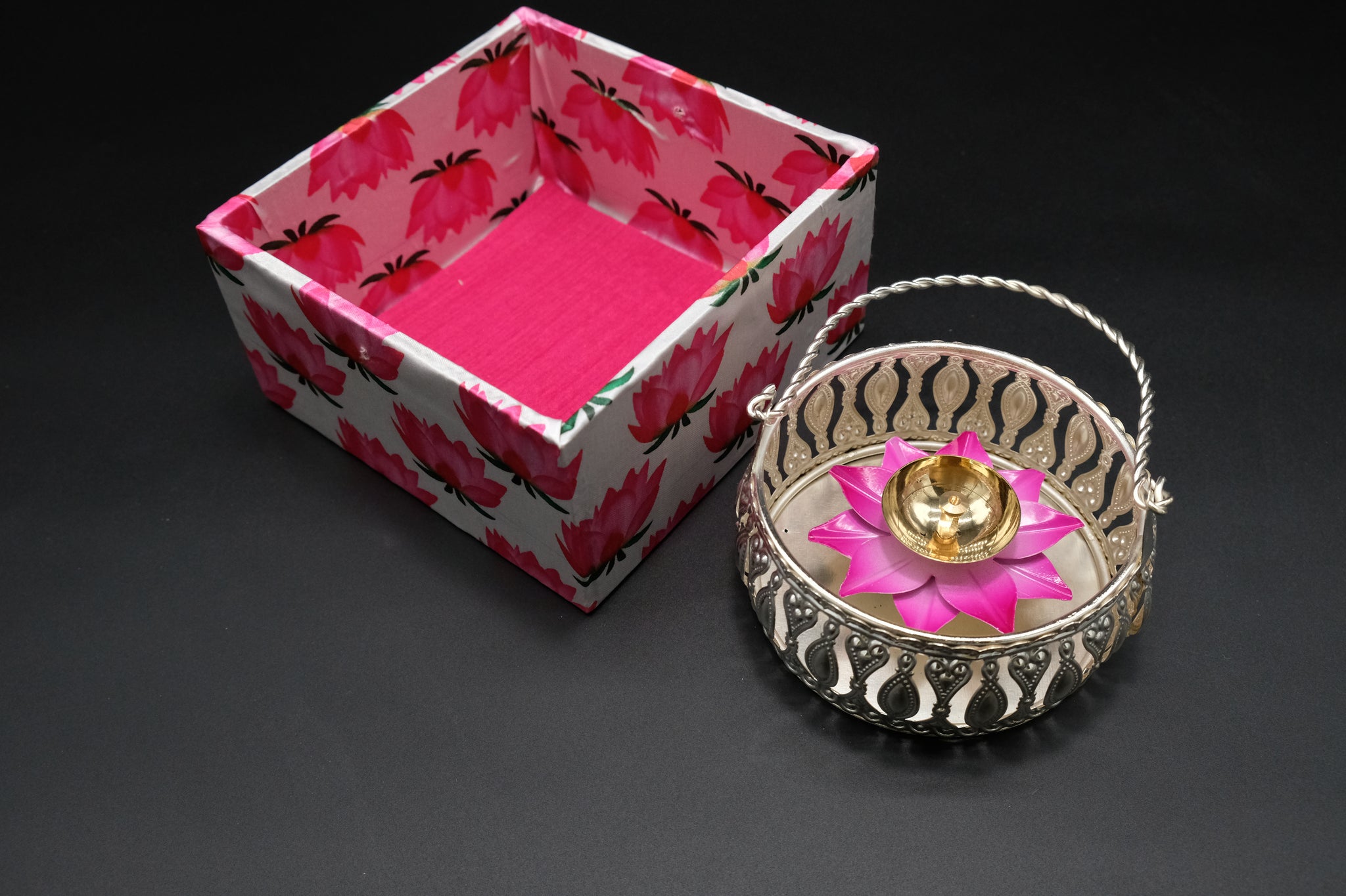 Premium Diwali favor gift basket with silver lattice cutwork and twisted handle displaying brass lotus diya with pink enamel petals