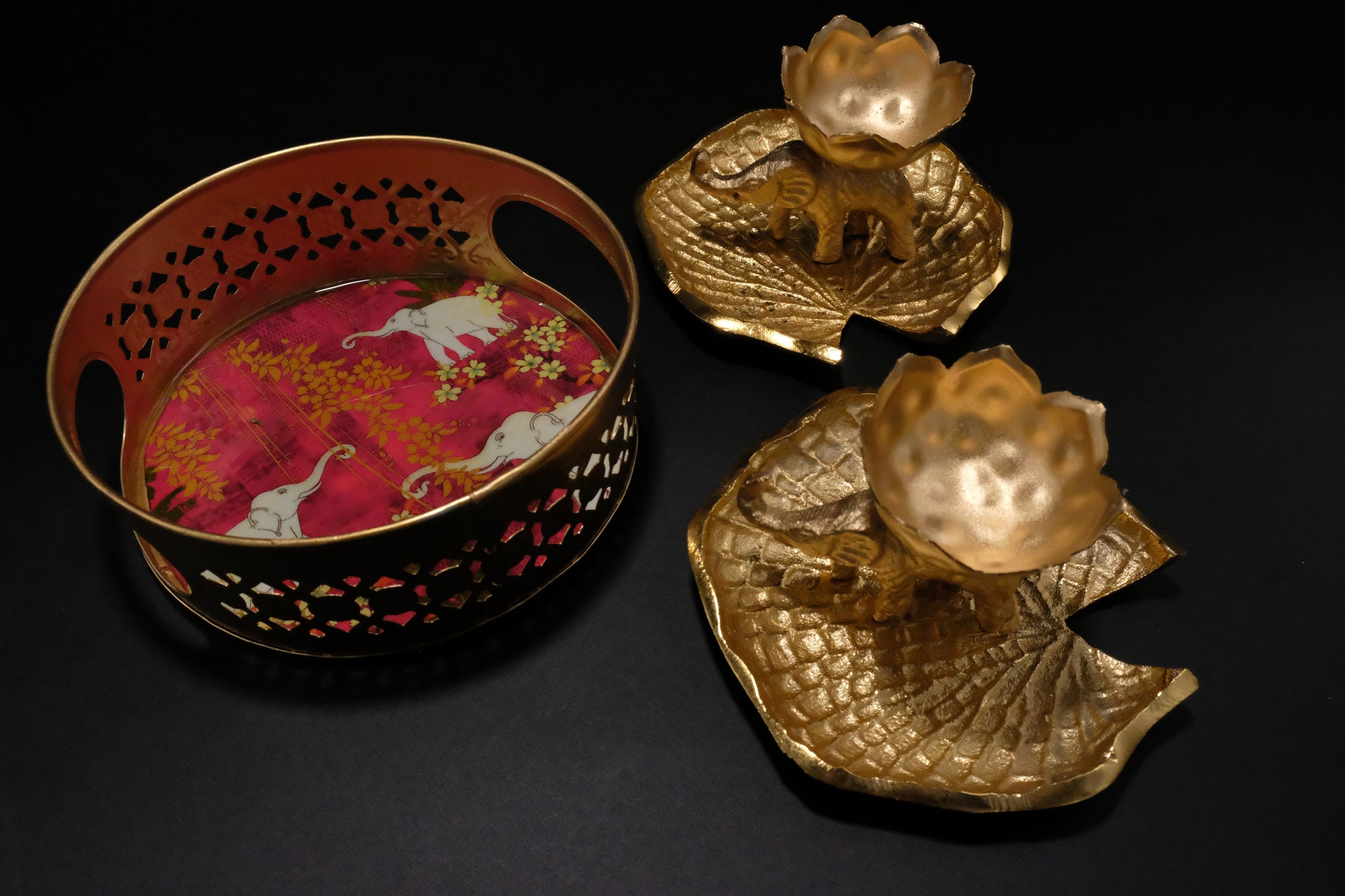 Close up detail of elephant diya holders and decorative coasters from premium Diwali gift set showing gold metallic finish and traditional patterns