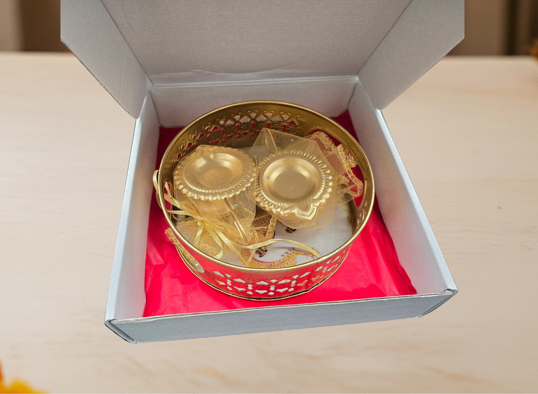 Diwali favor gift showing decorative gold lattice tray with two traditional gold leaf diyas in elephant print gift box with red lining