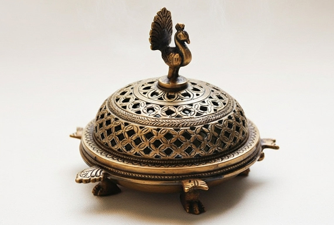 A three-quarter view of the handcrafted brass bakhoor burner, showing its round shape, intricate latticework, and the elegant peacock finial on the removable lid